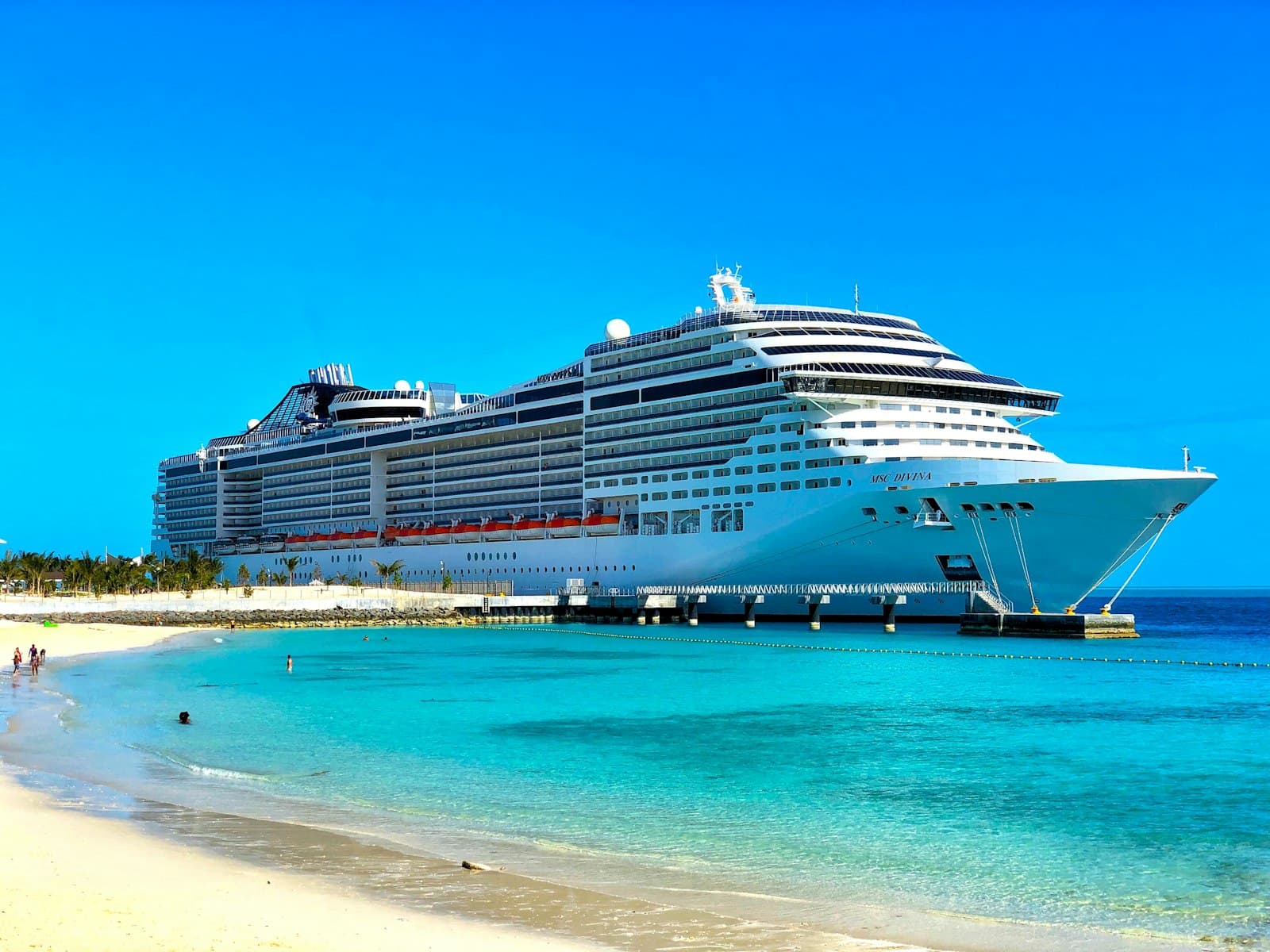 A white cruise ship docked next to a sandy beach