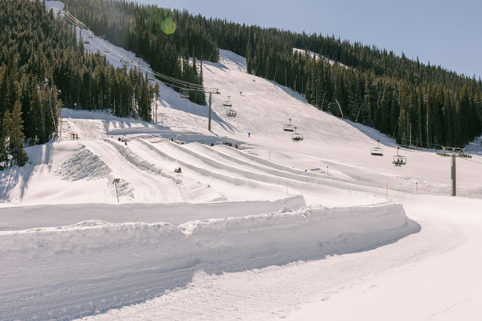 Chairlifts above a snow-covered ski slope lined with pine trees