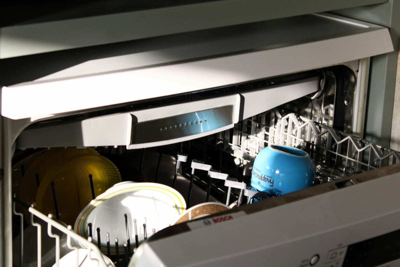 An open dishwasher with plates and a mug loaded in the racks