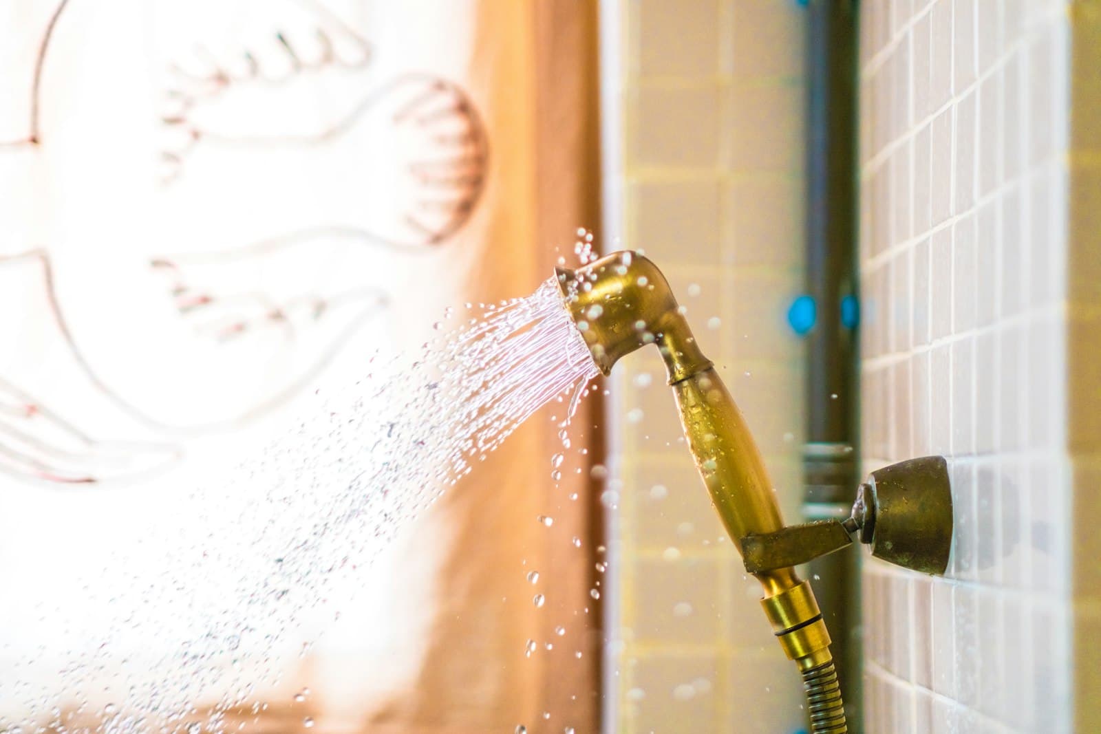 A hand shower spraying hot water against a tiled bathroom wall