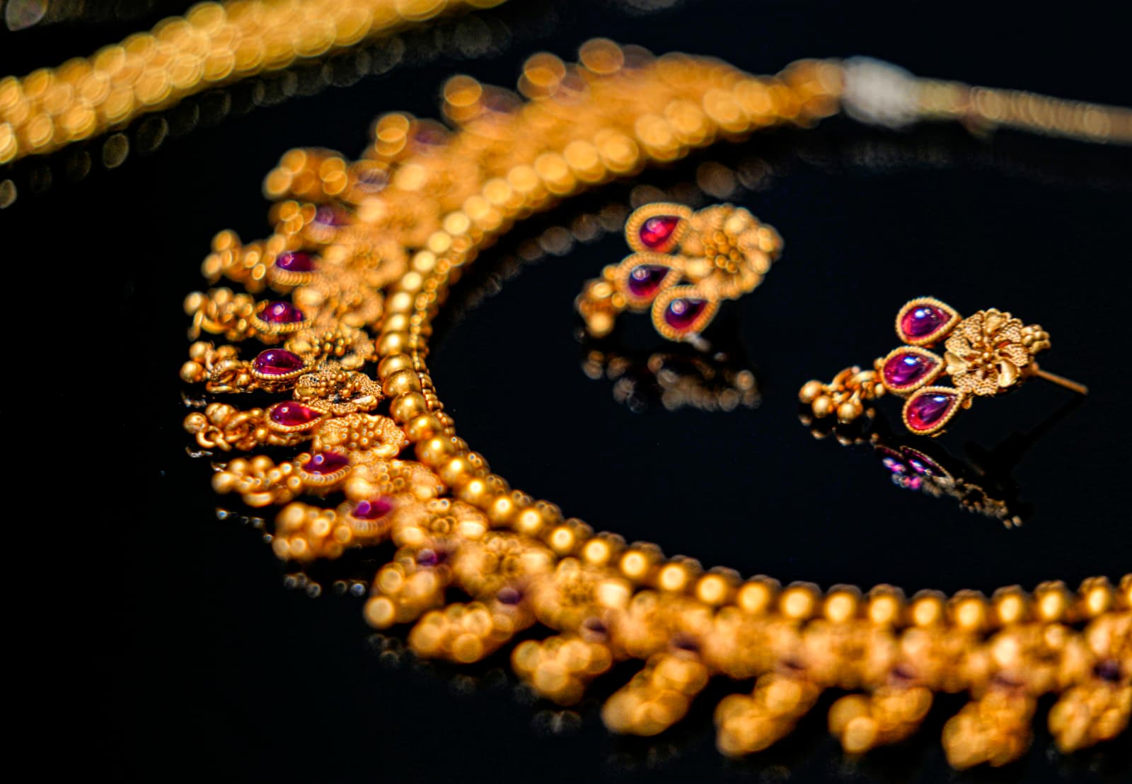 A gold necklace and matching earrings on a dark reflective surface
