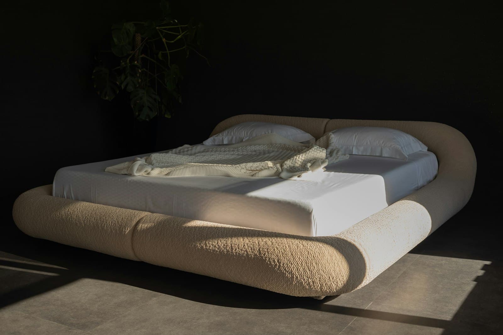 A mattress on an upholstered platform bed in soft window light